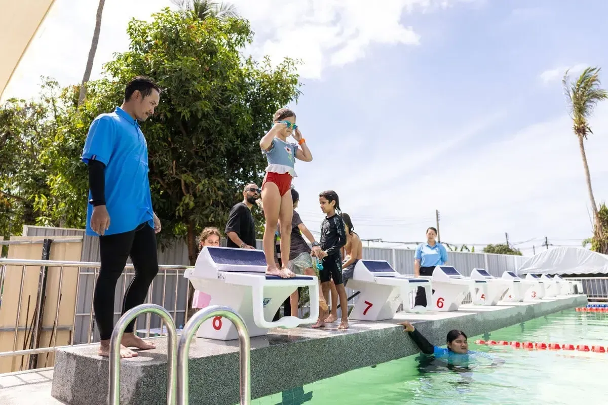 A coach helping a young swimmer at the starting blocks